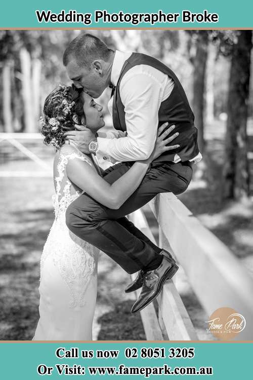 Photo of the Groom sitting on the fence while kissing the Bride on the forehead Broke NSW 2330