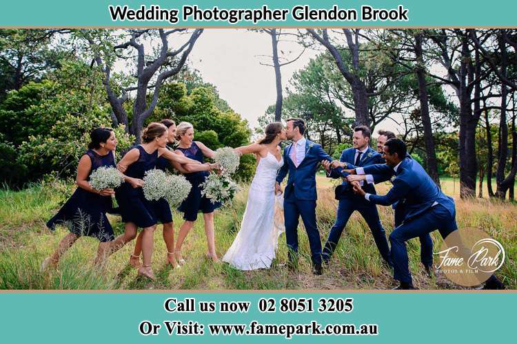 Photo of the Bride and the Groom kissing while teasing by the entourage Glendon Brook NSW 2330