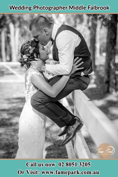 Photo of the Groom sitting on the fence while kissing the Bride on the forehead Middle Falbrook NSW 2330